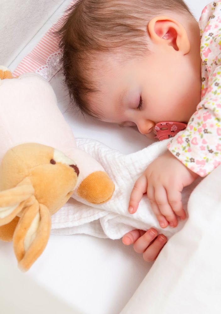 Baby girl sleeping in a cot with pacifier and toy