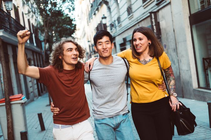 Cheerful multiracial friends hugging and walking along city street