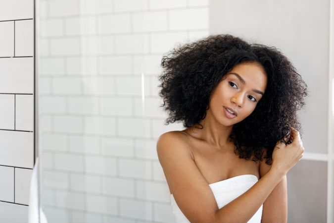 Black woman touching her hair in bathroom with towel wrapped around her