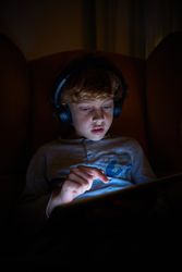 Boy playing game on tablet in darkness