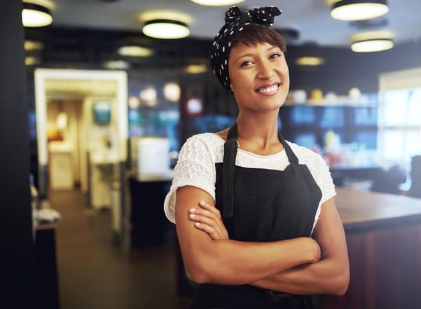 Black woman standing and smiling in a restaurant with her arms crossed