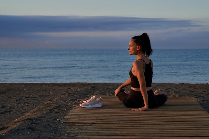 Hispanic woman sitting in Parivritta Sukhasana posture on coast