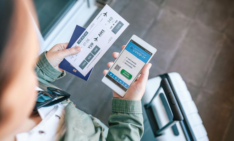 Unrecognizable woman holding cell phone with covid passport and boarding pass