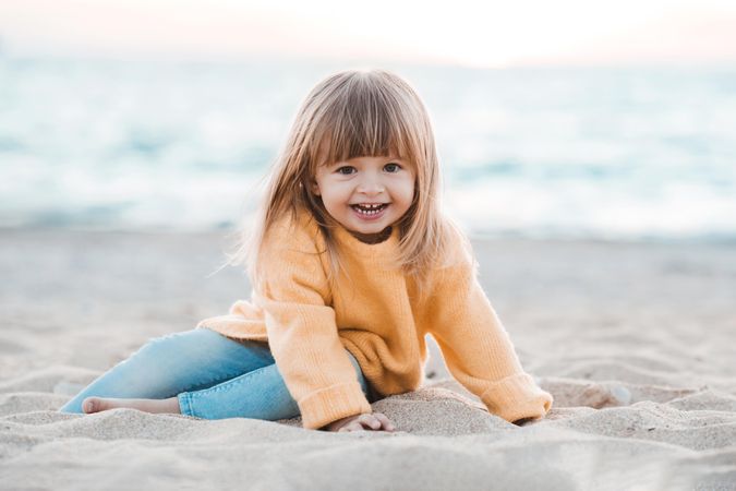 Smiling girl in yellow sweater sitting on sandy beach