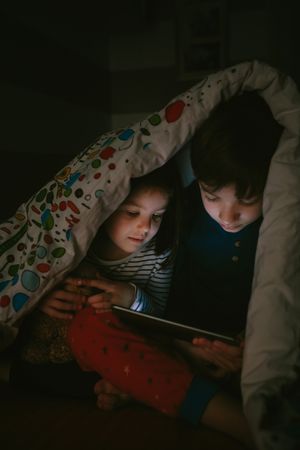 Siblings looking at the tablet in the dark