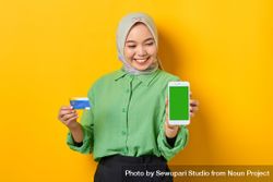 Happy Muslim woman in headscarf and green blouse holding credit card and smart phone screen mock up 4meAo4