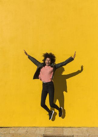 Black woman with afro hair jumping for joy in the street.