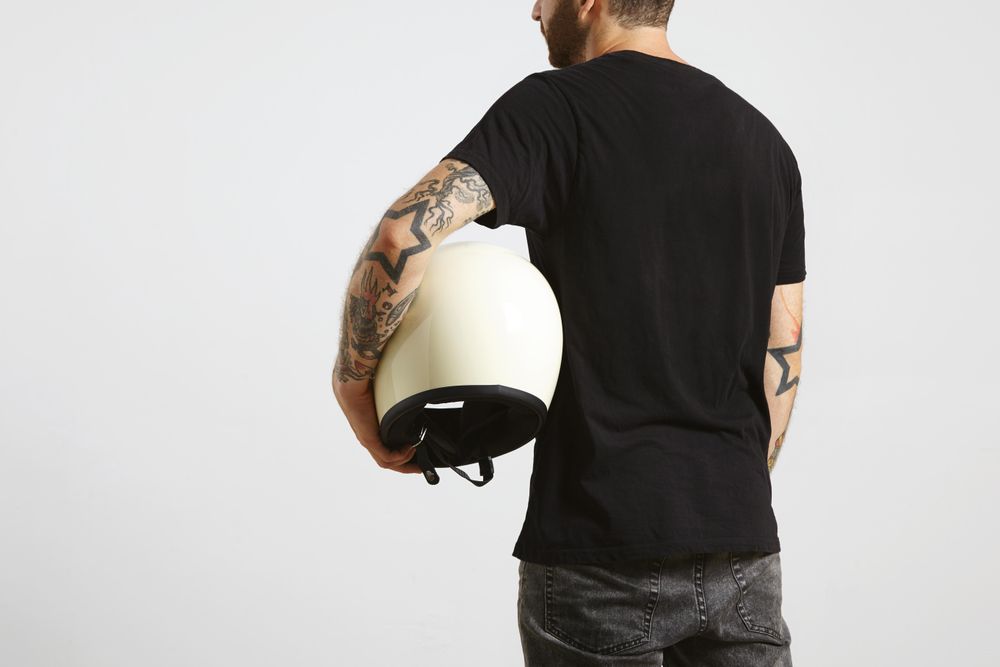 Rearview of man in plain dark t-shirt and dark jeans with motorcycle helmet under arm