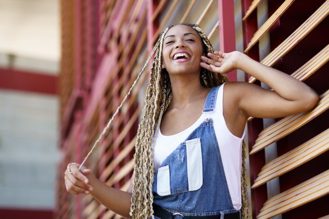Laughing female in vest and overalls posing on window blinds