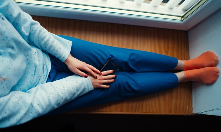 Crop woman in home clothes on window sill