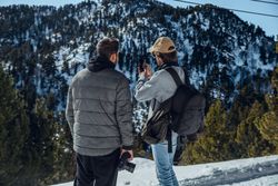 Men with smartphone and camera on hill between trees in winter