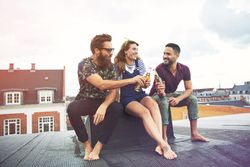 Relaxed group of barefoot friends toasting beers on a rooftop