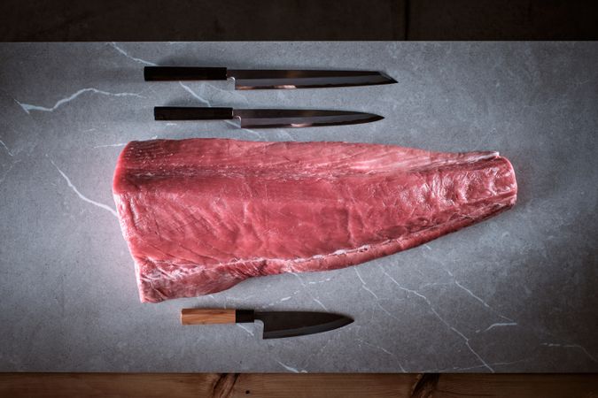 Bluefin tuna loin on a cement background with three knives