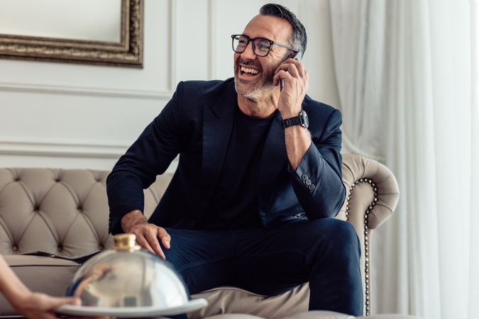 Cheerful businessman talking on mobile phone in hotel room