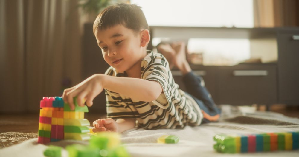 Portrait of Cute Male Asian Child Playing with Colourful Building Blocks in his Room During the Day.