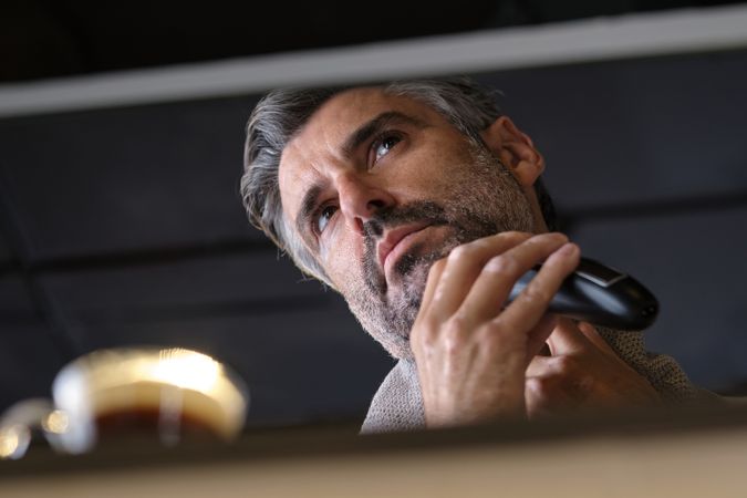 Adult man trimming beard and looking away