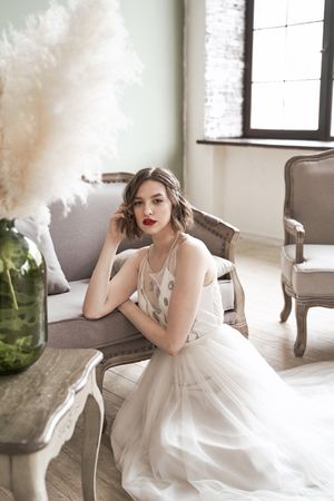 woman with red lips in white dress looking at camera while sitting on floor beside sofa