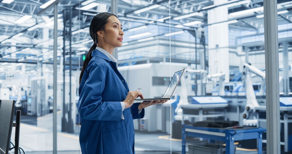 Southeast Asian Engineer Using Laptop Computer and Looking Around a Factory Facility with Equipment Producing Modern Electronic Components for Advanced Industrial Productions