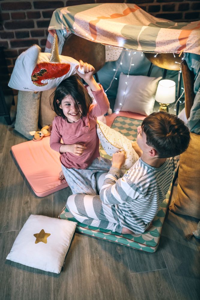 Cheerful boy and girl with pajama laughing and playing in cushion battle at home in front of tent