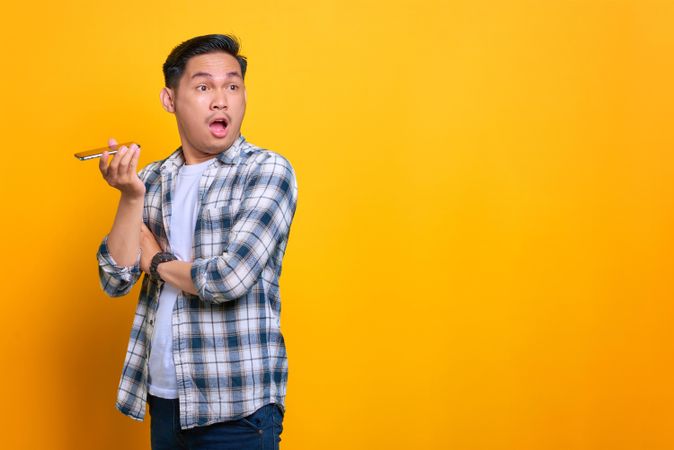 Asian male amazed while using speaker phone in studio shoot with copy space