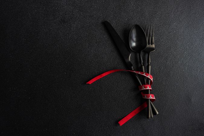 Dark cutlery on dark background tied with bright red ribbon