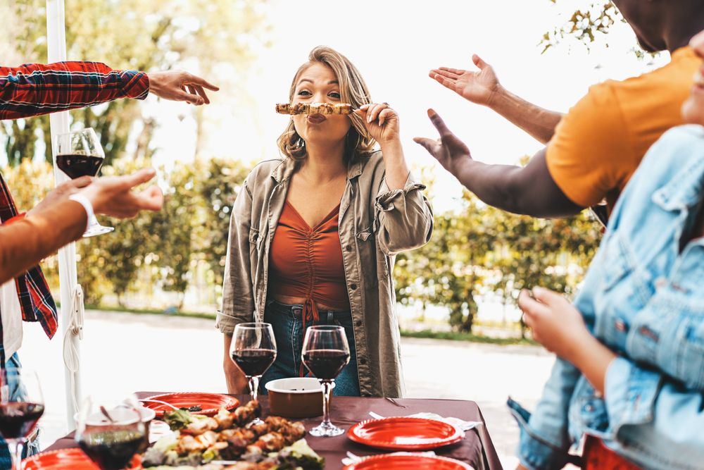 Friends having fun party with a woman making a funny face holding skewers grilled on barbecue