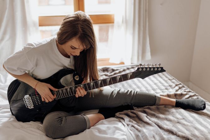 side view of Young brunette woman playing guitar on bed