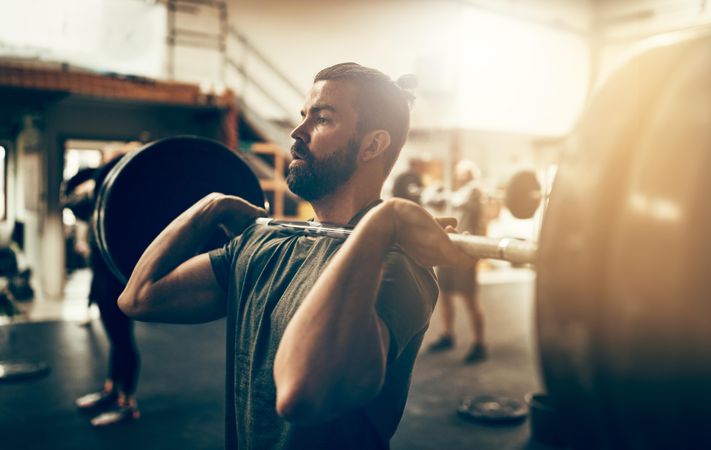 Focused man holding heavy barbell on shoulders