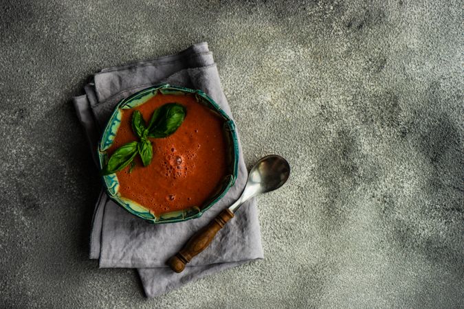 Top view of traditional Spanish tomato soup Gazpacho with basil on grey napkin with copy space
