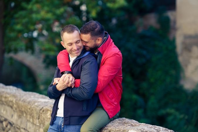 Cute gay couple holding each other by the river, copy space with sun flare