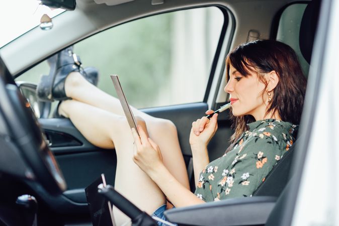 Curious female wearing floral shirt and shorts writing notes while sitting in parked car