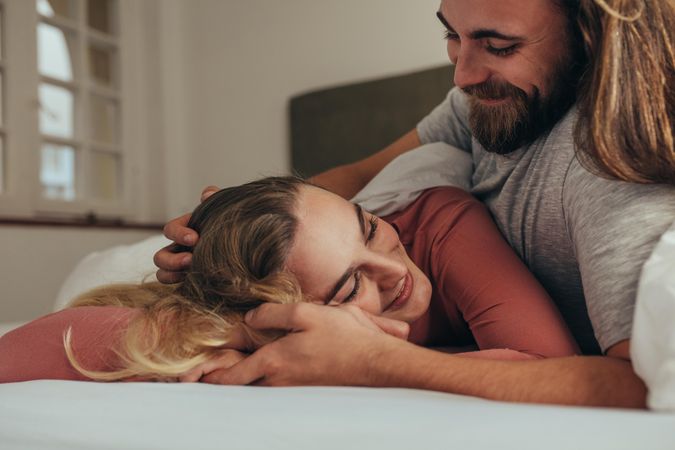 Smiling man lying on bed with his wife holding hands and loving her