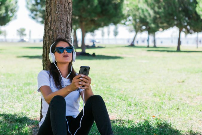 Relaxed trendy woman in headphones resting in park on grass