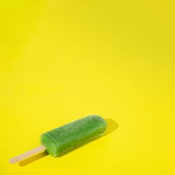 Green ice pop lying on yellow background