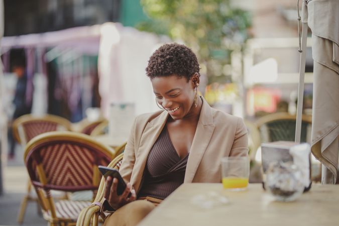 Smiling Black woman with smartphone sitting at table near luggage in cafe