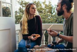 Couple sharing a pizza sitting in the balcony of their apartment 481Pjb