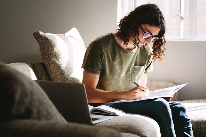 Focused college student taking notes while taking online class from home
