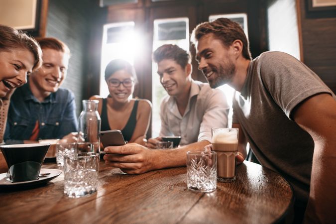 Group of friends sitting around a cafe table and looking at mobile phone