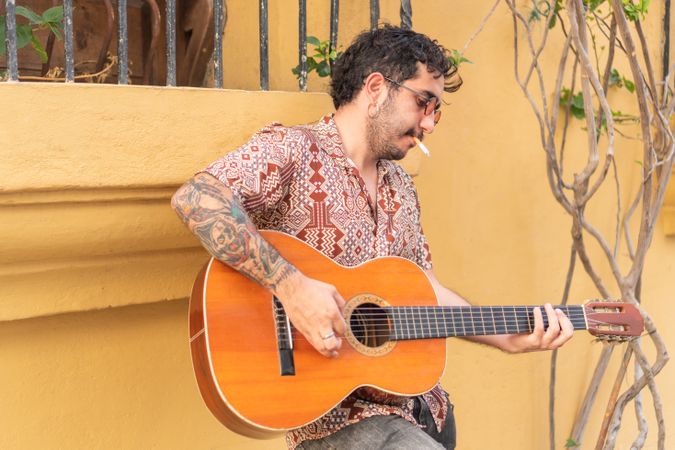 Young man with guitar playing guitar while smoking. Guitarist standing in the street.