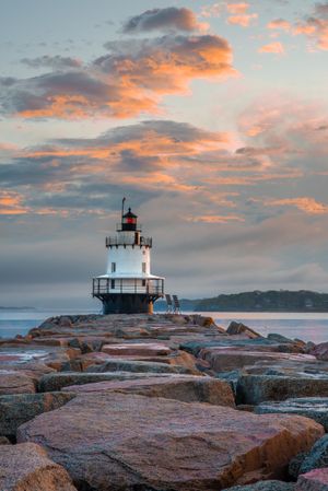 Lighthouse on rocks near ocean during sunset