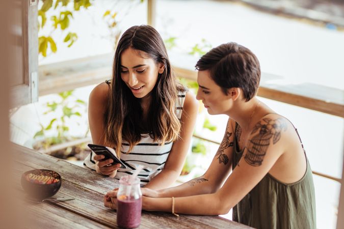 Two women sitting at a cafe looking at a mobile phone