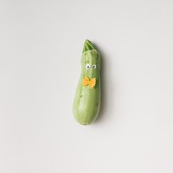 Zucchini with googly eyes and bowtie pasta on light background