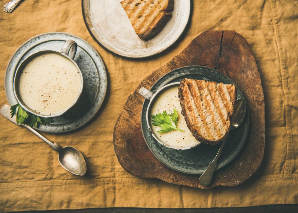 Top view of two cups of celery soup with toast, and spoon, on wooden board