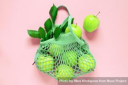 Mesh bag of bright green apples on pink background 0vdzZ4