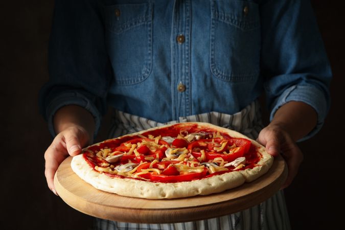 Woman hold raw pizza on brown background