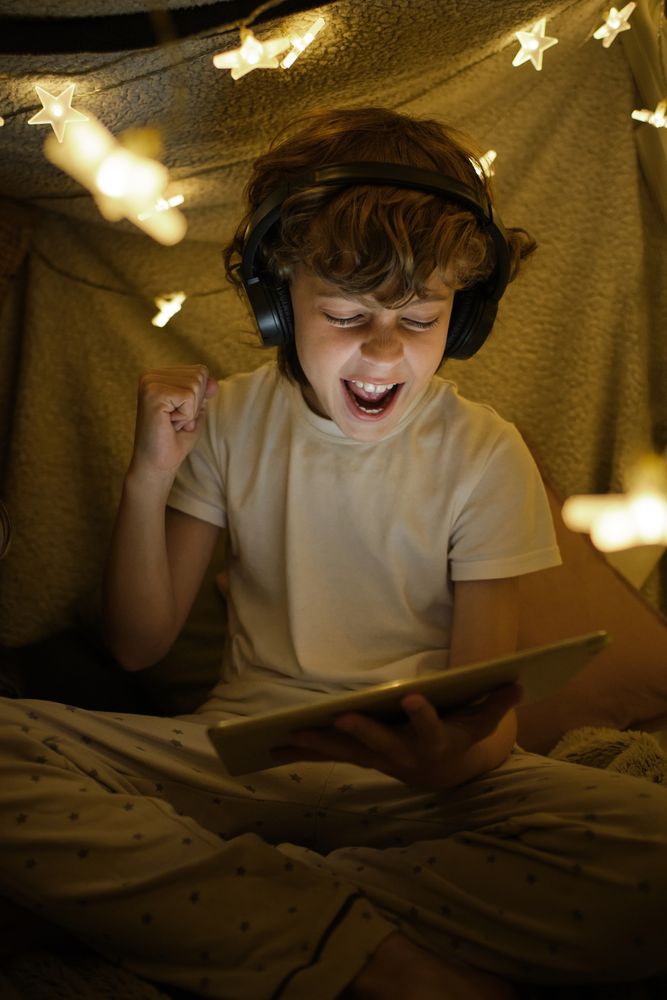 Cheerful boy watching match on tablet in blanket fort