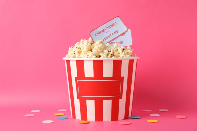 Confetti, bucket with popcorn and tickets on pink background, copy space