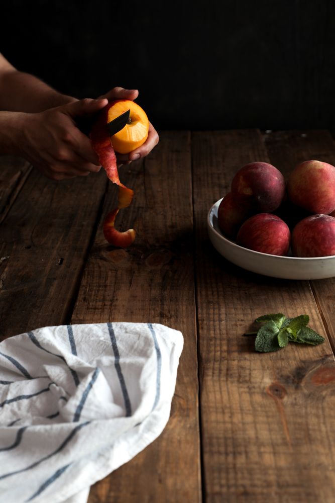 Tasty ripe peaches in plate and hands peeling peach