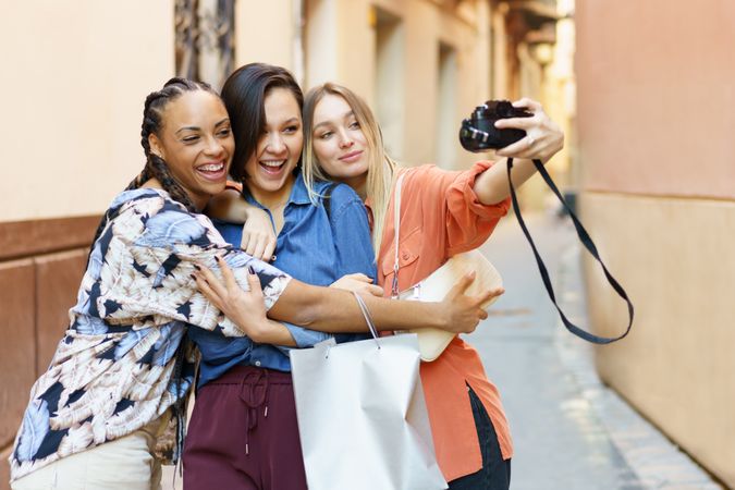 Three smiling women in narrow lane taking selfie with camera