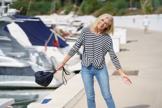 Older woman in jeans and striped shirt swinging around her bag outside on dock